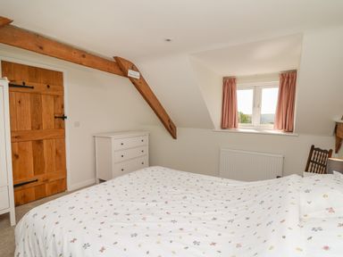 A bedroom with a bed, wooden door, white dresser, window with curtains and wooden beams at Cattle Tree Cottage Llangoedmor near Cardigan