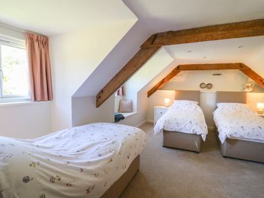 A bedroom with three single beds floral bedding two bedside tables lamps wooden beams on ceiling at Cattle Tree Cottage in Llangoedmor near Cardigan