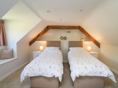 A bedroom with two single beds under a wooden beam and bedside tables with lamps at Cattle Tree Cottage in Llangoedmor near Cardigan