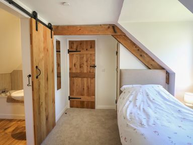 A bedroom with a bed with patterned bedding next to wooden doors and exposed wooden beams at Cattle Tree Cottage Llangoedmor near Cardigan