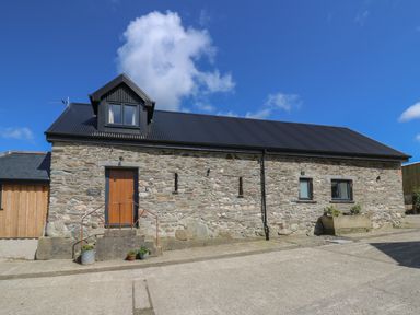 Exterior view of a stone building with a black roof and wooden door at Cattle Tree Cottage in Llangoedmor near Cardigan
