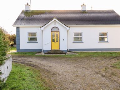 A single-story house with a yellow front door and three windows with blinds at 17 Buninver Road in Gortin