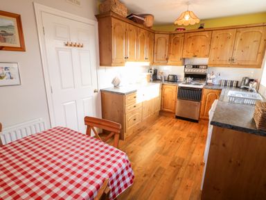 A kitchen with wooden cabinets a stove a sink and a table with a red and white checkered tablecloth at 17 Buninver Road Gortin