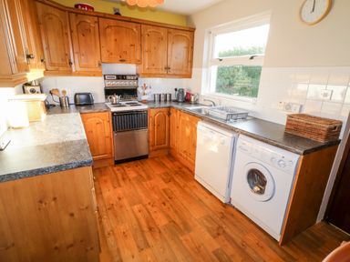 A kitchen with wooden cabinets and flooring a stove dishwasher washing machine and a window at 17 Buninver Road in Gortin