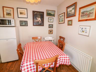 A dining area with a red and white checkered tablecloth on a table surrounded by wooden chairs fridge and microwave on the left wall and framed pictures on the walls at 17 Buninver Road in Gortin