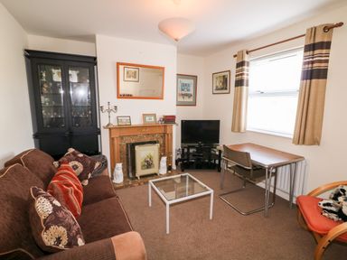 A living room with a brown sofa cushions a glass coffee table a wood desk a TV a fireplace and a display cabinet at 17 Buninver Road in Gortin