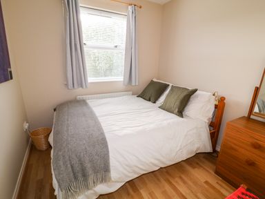 A bedroom with a bed with green pillows a grey blanket a wooden dresser and a window with curtains at 17 Buninver Road in Gortin