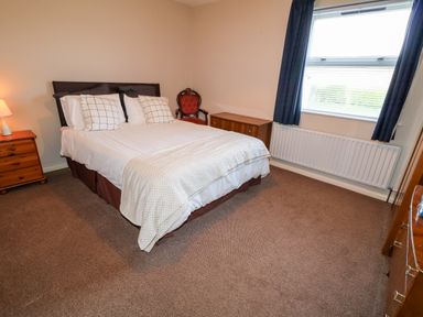 A bedroom with a double bed bedside table with a lamp a wooden chair a dresser and a window with blinds and curtains at 17 Buninver Road in Gortin
