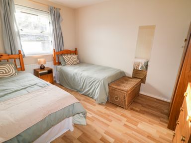 A bedroom with two single beds a bedside table with a lamp a wicker chest a wall mirror and a wooden wardrobe at 17 Buninver Road in Gortin