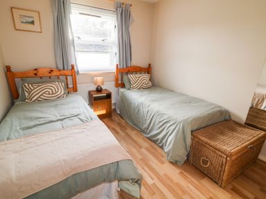 A bedroom with two single beds a nightstand with a lamp a window with curtains a wicker storage basket and a wall mirror at 17 Buninver Road in Gortin