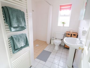 A bathroom with a shower area towels on a radiator toilet sink and a window with a pink blind at 17 Buninver Road in Gortin