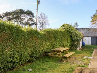 A wooden picnic table on grass beside a tall hedge with trees and a building in the background at 17 Buninver Road in Gortin