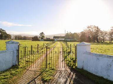 A driveway with an iron gate leading to a white house surrounded by green fields at 17 Buninver Road in Gortin