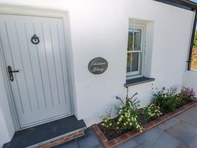 A white cottage exterior with a gray door a window and a flower bed at Catamouse in Milford Haven