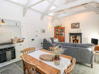 A living room with wooden dining table and chairs gray sofas fireplace and kitchen area at Catamouse in Milford Haven