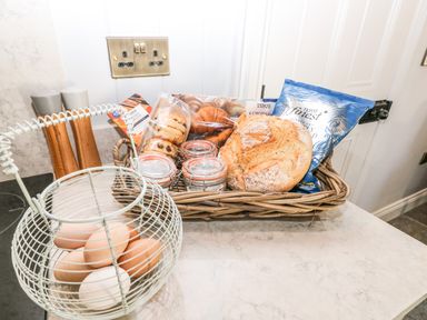 A kitchen counter with a basket of eggs and a wicker basket containing bread cookies croissants and jars at Catamouse in Milford Haven