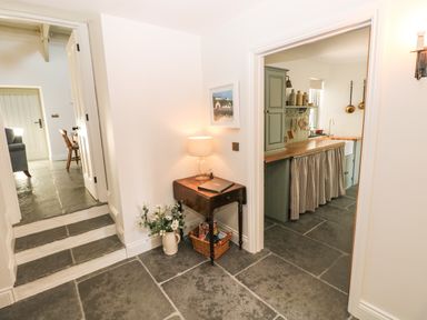 A hallway with stone tile flooring small table with a lamp and flower vase next to two doorways one leading to a kitchen with wooden countertop and green cabinets at Catamouse in Milford Haven