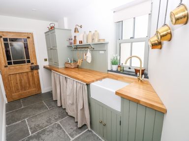 A laundry room with a wooden door a farmhouse sink wooden countertops and brass pots hanging on the wall at Catamouse in Milford Haven