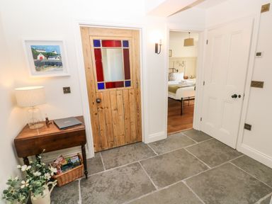 A hallway with a wooden door with stained glass panels a small table with a lamp and a basket with magazines a doorway leading to a bedroom at Catamouse in Milford Haven