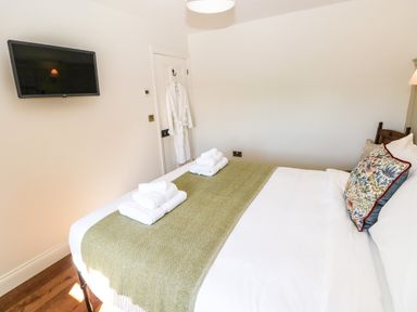 A bedroom with a bed with white linens and green runner with towels on top and a wall mounted tv at Catamouse in Milford Haven