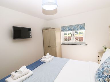 A bedroom with a bed covered with blue and white linens two sets of folded white towels a wall-mounted TV a beige wardrobe and a window with a blue floral curtain at Catamouse in Milford Haven