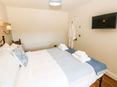 A bedroom with a made bed with folded towels a wall mounted television and a robe hanging on a door at Catamouse in Milford Haven