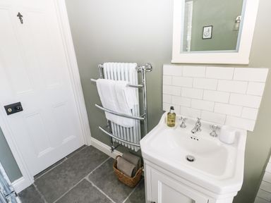 A bathroom with a white sink cabinet a mirror a towel radiator with white towels and a basket on the floor at Catamouse in Milford Haven