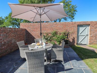 An outdoor patio with a round table and four chairs under a large umbrella and a brick wall at Catamouse in Milford Haven