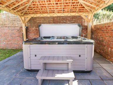A hot tub under a wooden gazebo with string lights on a paved patio at Catamouse in Milford Haven