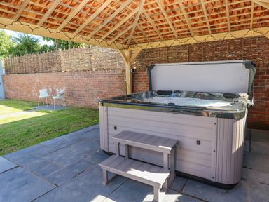 An outdoor covered patio area with a hot tub on a stone floor and two chairs with cushions on grass at Catamouse in Milford Haven