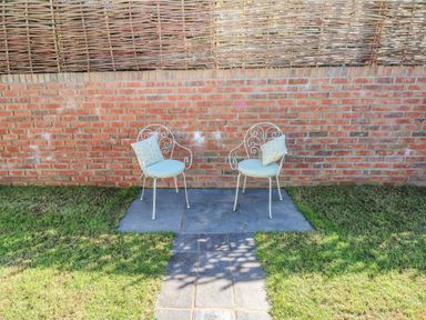 Two metal chairs with cushions on a patio area in a garden with a brick wall and woven fence behind at Catamouse in Milford Haven