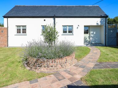 A white house with three windows a gray door and a brick circular planter with plants in a garden at Catamouse in Milford Haven