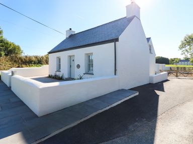 A white cottage with a blue door and slate roof surrounded by a low white wall at Catamouse in Milford Haven