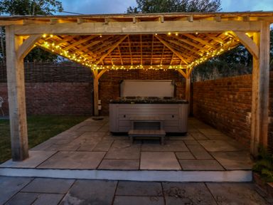 An outdoor wooden gazebo with string lights covering a hot tub and a small set of steps at Catamouse in Milford Haven