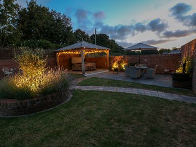 A garden with a gazebo, string lights, patio furniture with umbrella, and illuminated plants at Catamouse in Milford Haven