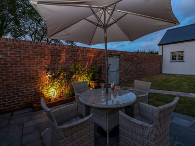 An outdoor patio area with a round glass table under a large umbrella with four wicker chairs and a brick wall with garden lighting at Catamouse in Milford Haven