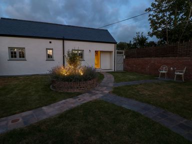 A garden with a paved path leading to a white building with an open door and two chairs near a brick wall at Catamouse in Milford Haven