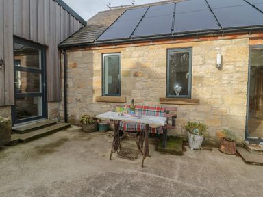 An outdoor patio area with an old sewing machine table and bench in front of a stone building with solar panels at High Barns Cottage Longhorsley near Morpeth