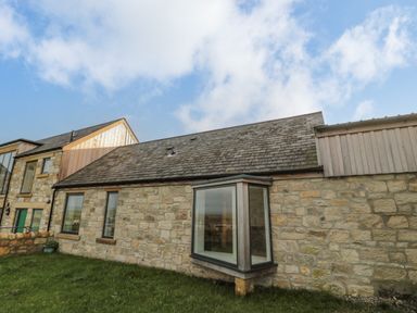 An exterior view of a stone house with multiple windows and a grass lawn at High Barns Cottage in Longhorsley near Morpeth