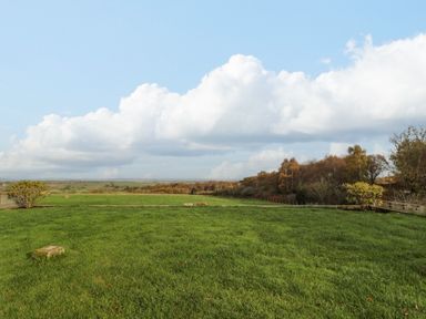 A grassy field with trees in the distance under a partly cloudy sky at High Barns Cottage in Longhorsley near Morpeth