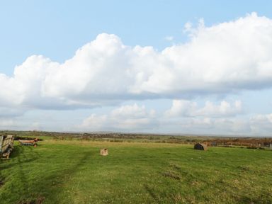 A green field with farm equipment and a fence under a cloudy sky at High Barns Cottage in Longhorsley near Morpeth