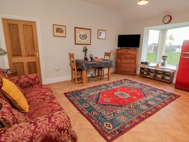 A living room with red patterned sofa yellow pillow wooden dining table chairs colorful rug wooden dresser and television at High Barns Cottage in Longhorsley near Morpeth
