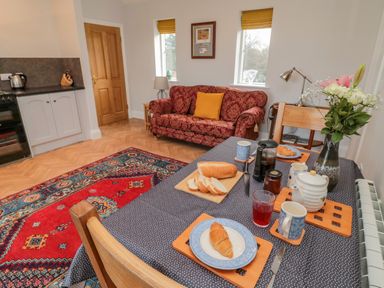 A dining area with a table set for breakfast and a red sofa in the background at High Barns Cottage in Longhorsley near Morpeth
