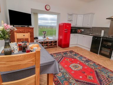 A kitchen with a dining table set with food a red refrigerator a wooden cabinet and a large window with a view at High Barns Cottage Longhorsley near Morpeth