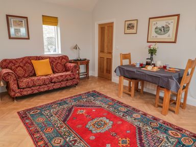 A living room with a patterned red sofa a wooden dining table set with food and a colorful rug at High Barns Cottage in Longhorsley near Morpeth