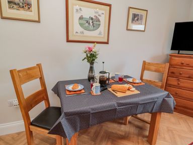 A dining table with two wooden chairs plates with croissants bread a French press a vase with flowers and framed pictures on the wall at High Barns Cottage in Longhorsley near Morpeth