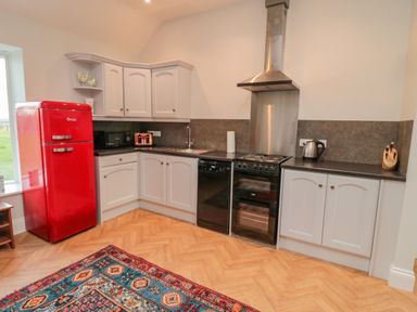 A kitchen with white cabinets a red refrigerator a stove dishwasher microwave kettle and a colorful rug on the floor at High Barns Cottage in Longhorsley near Morpeth