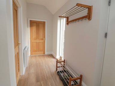A hallway with wooden doors a wall-mounted coat rack a shoe rack and a window at High Barns Cottage in Longhorsley near Morpeth