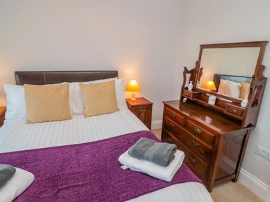 A bedroom with a bed, nightstand with lamp, and wooden dresser with mirror at High Barns Cottage in Longhorsley near Morpeth