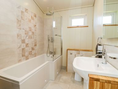 A bathroom with a bathtub shower combo a sink and a small window at Robin Lodge in Gargrave